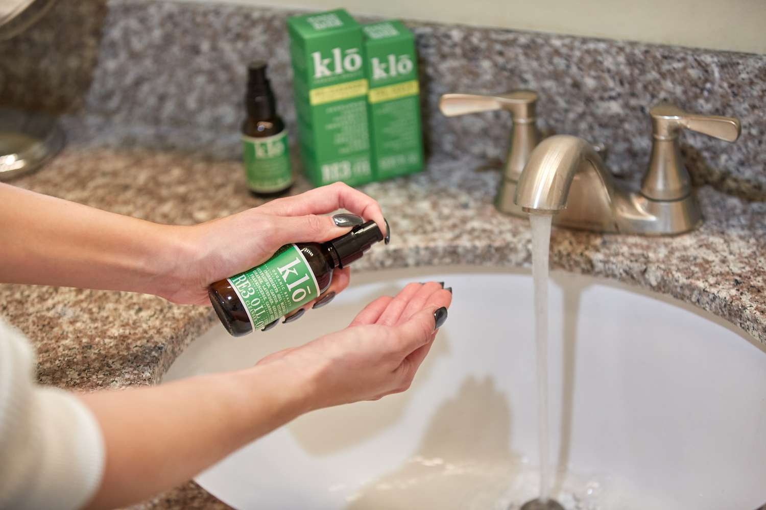 Klo Organic Beauty RE3 oil cleanser being pumped into hands at sink with water running.